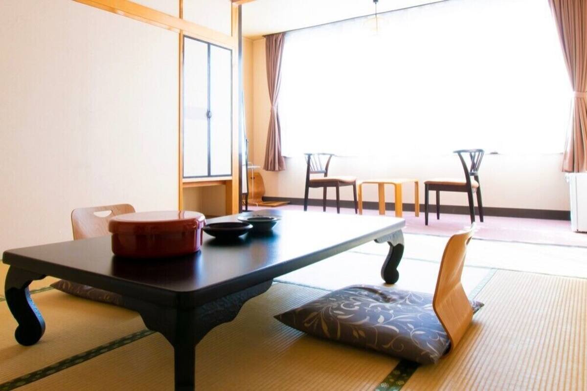 Ein traditioneller japanischer Raum mit Tatami-Böden, einem niedrigen Tisch und einem roten Behälter sowie zwei Stühlen.