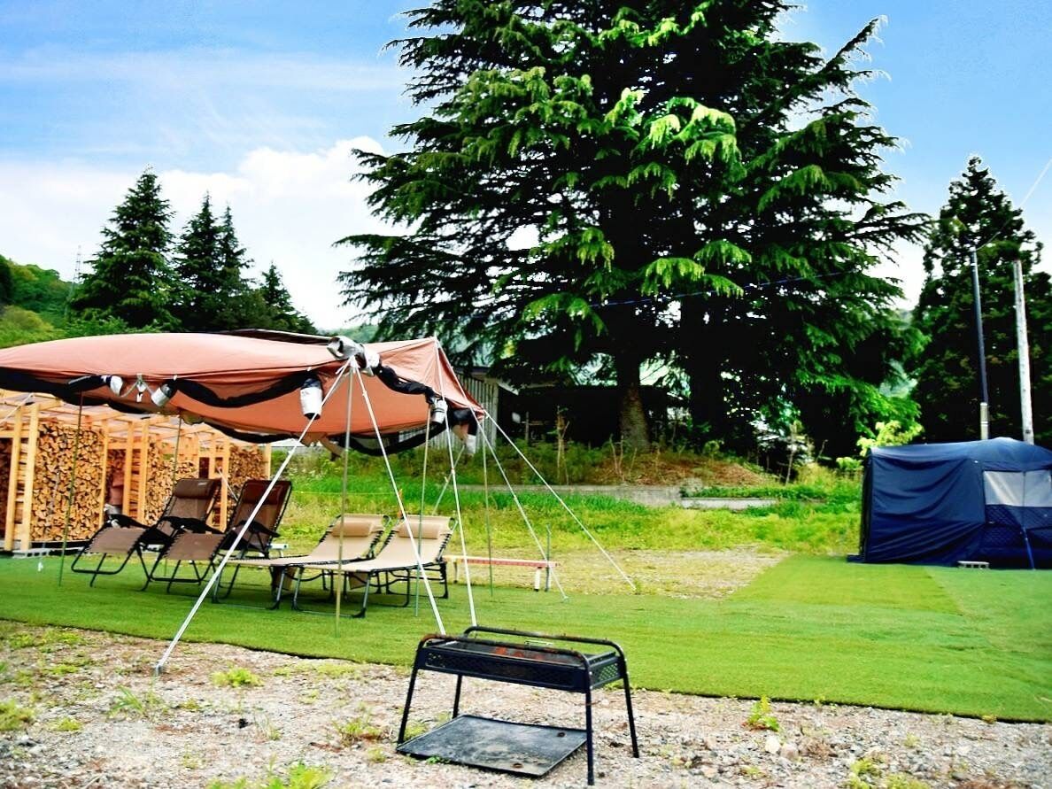 A campsite with a tent, a canopy, and a grill.