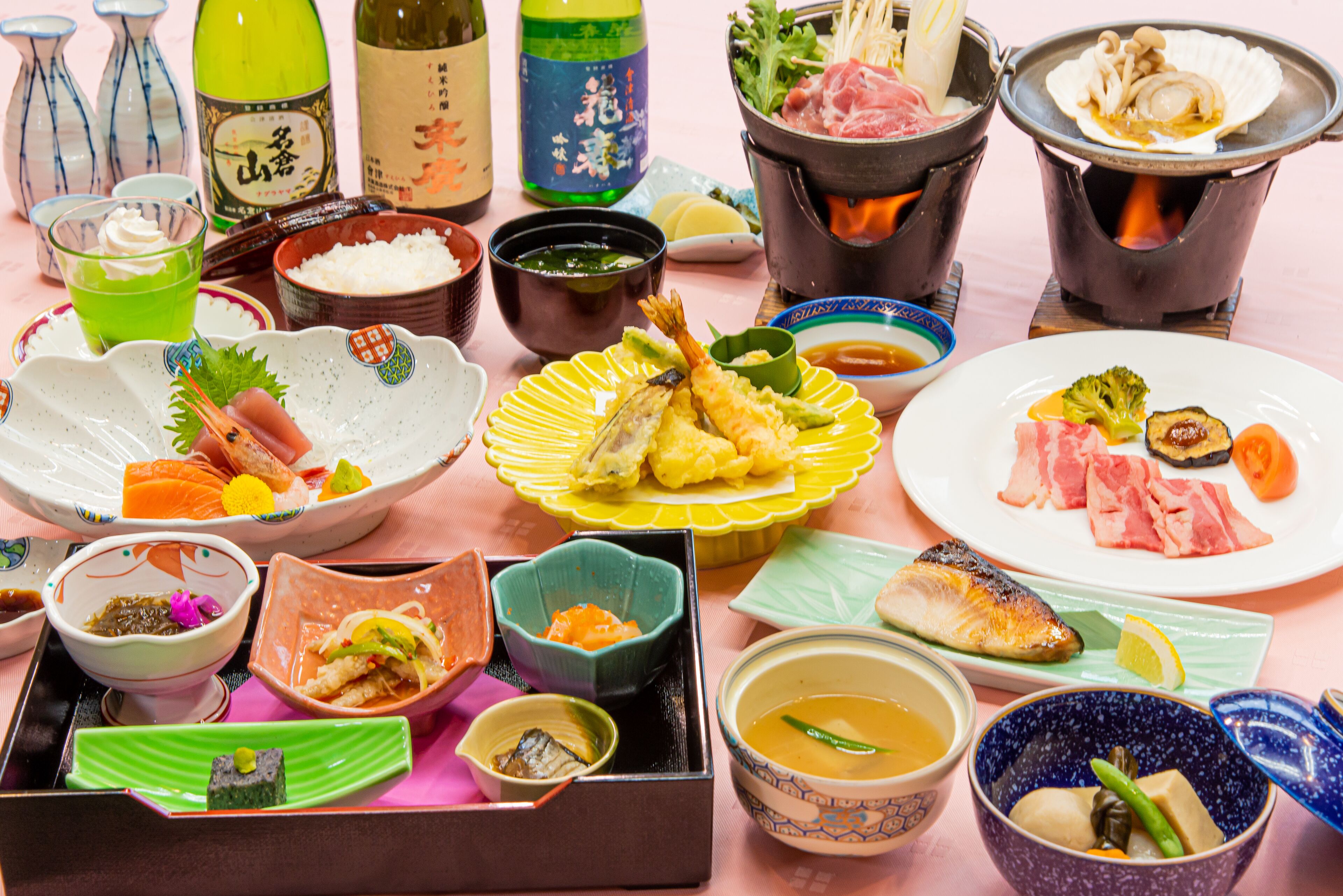 Variedad de platos japoneses, como sushi, sashimi y tempura, servidos sobre una mesa rosa con varios acompañamientos y salsas.