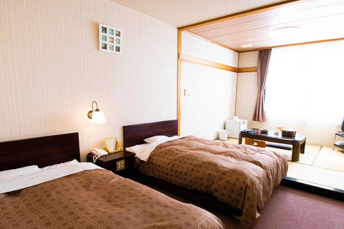 Ein Hotelzimmer mit zwei Betten, einem Nachttisch mit Lampe, einem kleinen Tisch mit Stuhl und einem großen Fenster mit Blick.