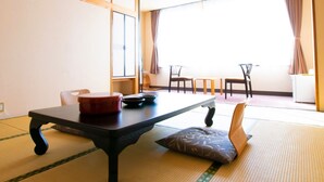 A traditional Japanese room with tatami flooring, a low table with a red container, and a view of the outside through large windows. - Ashinomaki Prince Hotel (Aizuwakamatsu)