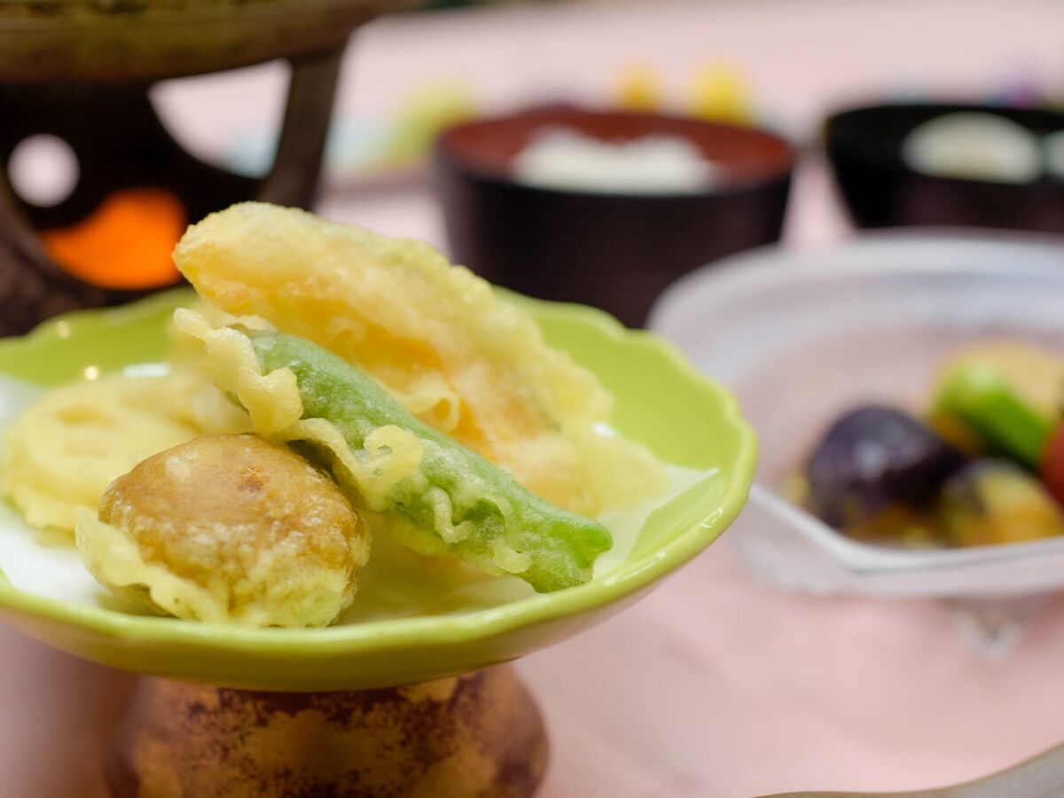 A bowl of food with a green plate, including a green vegetable and a round item.