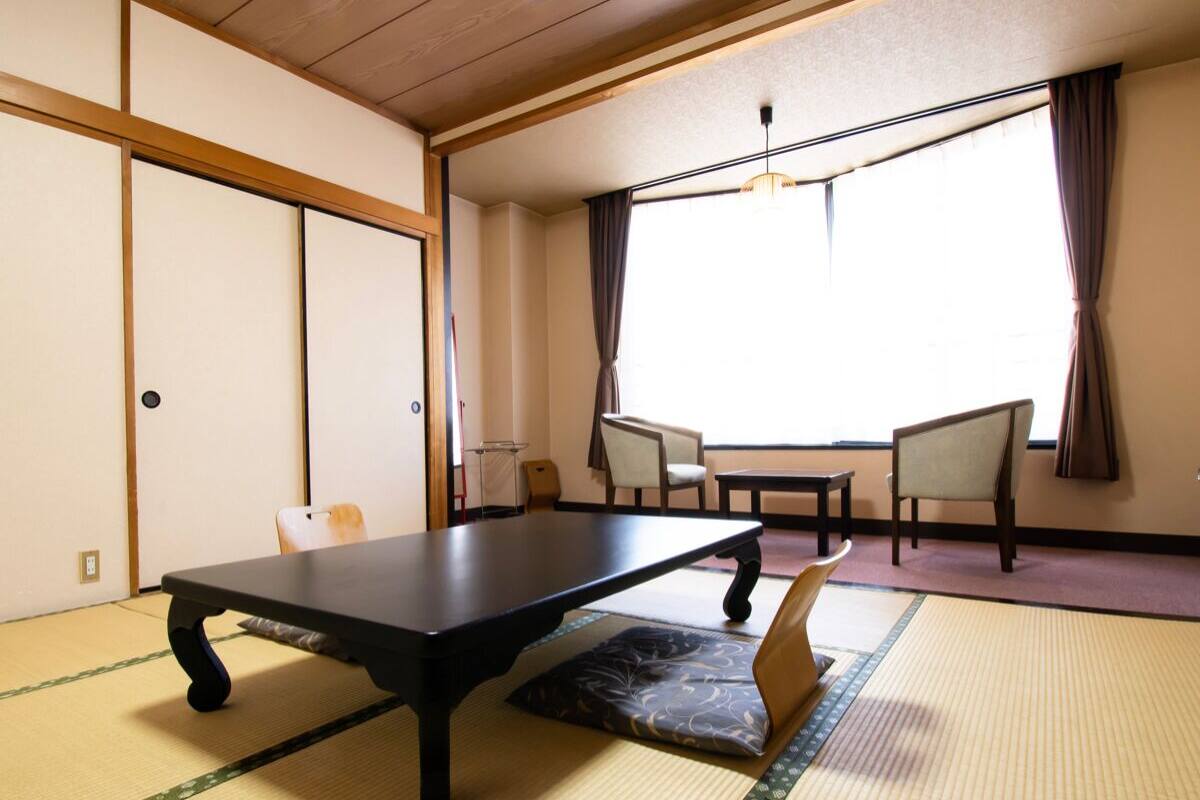 Ein traditioneller japanischer Raum mit Tatami-Boden, einem niedrigen Tisch, zwei Stühlen und einer Schiebetür.