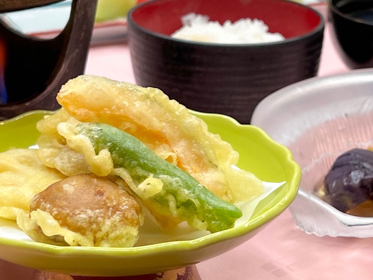 A bowl of tempura with vegetables and a small container of pickled plum.