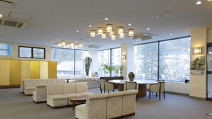 A spacious lobby with a seating area, a dining table, and large windows offering a view of the outside. - Ashinomaki Prince Hotel (Aizuwakamatsu)