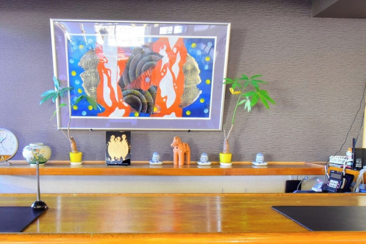 Een receptiebalie met daarboven een lijst, een klok en diverse potplanten.