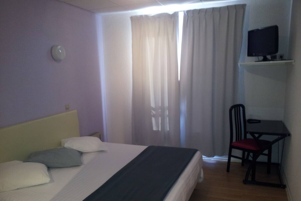 Une chambre d’hôtel équipée d’un lit, d’un bureau, d’une chaise, d’une télévision et d’une fenêtre avec des rideaux.