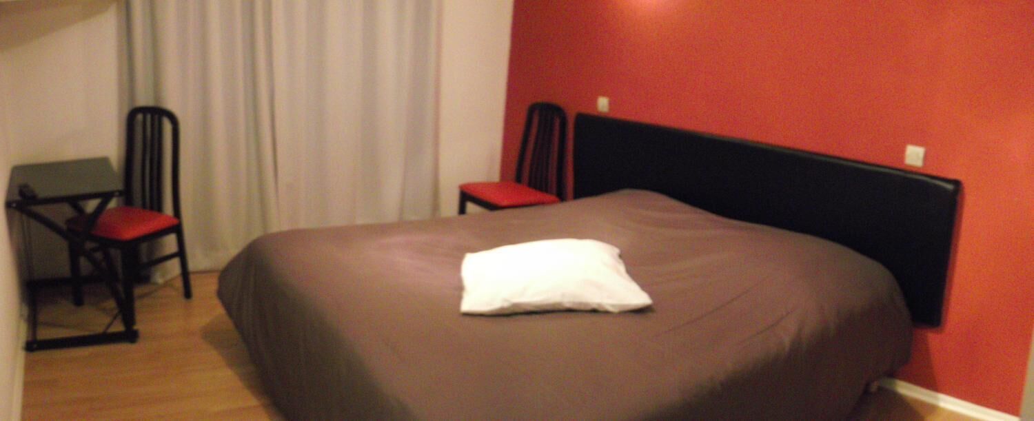 Une chambre d’hôtel avec un grand lit, un bureau, deux chaises et un mur rouge.
