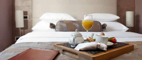 A neatly made bed with white linens and pillows, a bedside table with a tray containing a teapot, cups, a glass of orange juice, and some food items.
