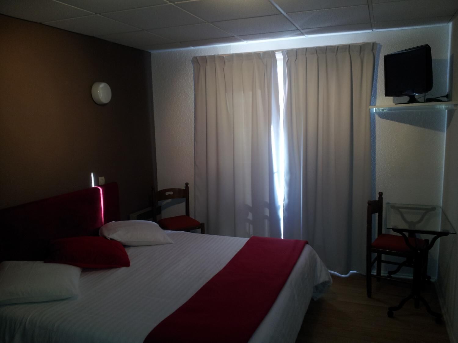 Une chambre d’hôtel avec un lit, une chaise, un bureau, une télévision et une fenêtre avec des rideaux.