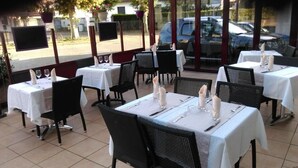 Un espace de restauration en plein air avec des tables pour deux, agrémenté de nappes blanches et de chaises en osier noir.