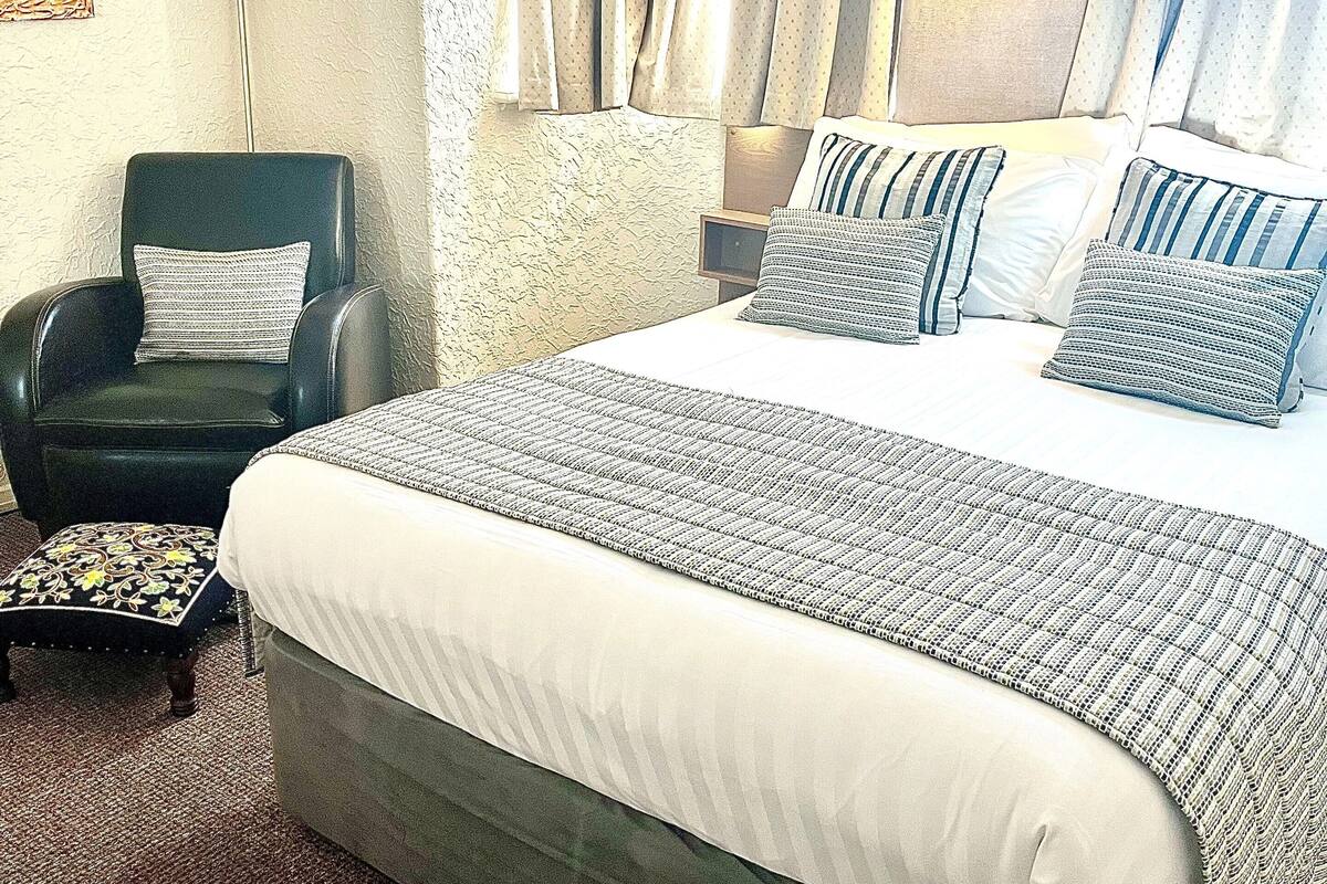 A hotel room with a large bed, a chair, a lamp, and curtains.