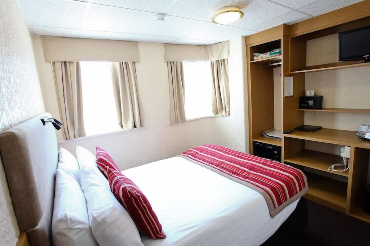 A hotel room with a bed, curtains, a television, and a desk with a computer.