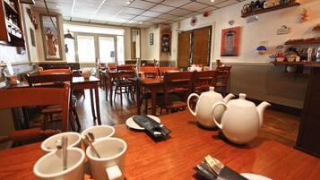 A dining area with wooden tables and chairs, white teapots, and a kitchen counter with various items.