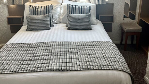 Una habitación de hotel con una cama grande, dos mesitas de noche, una lámpara, un espejo y una ventana con cortinas.
