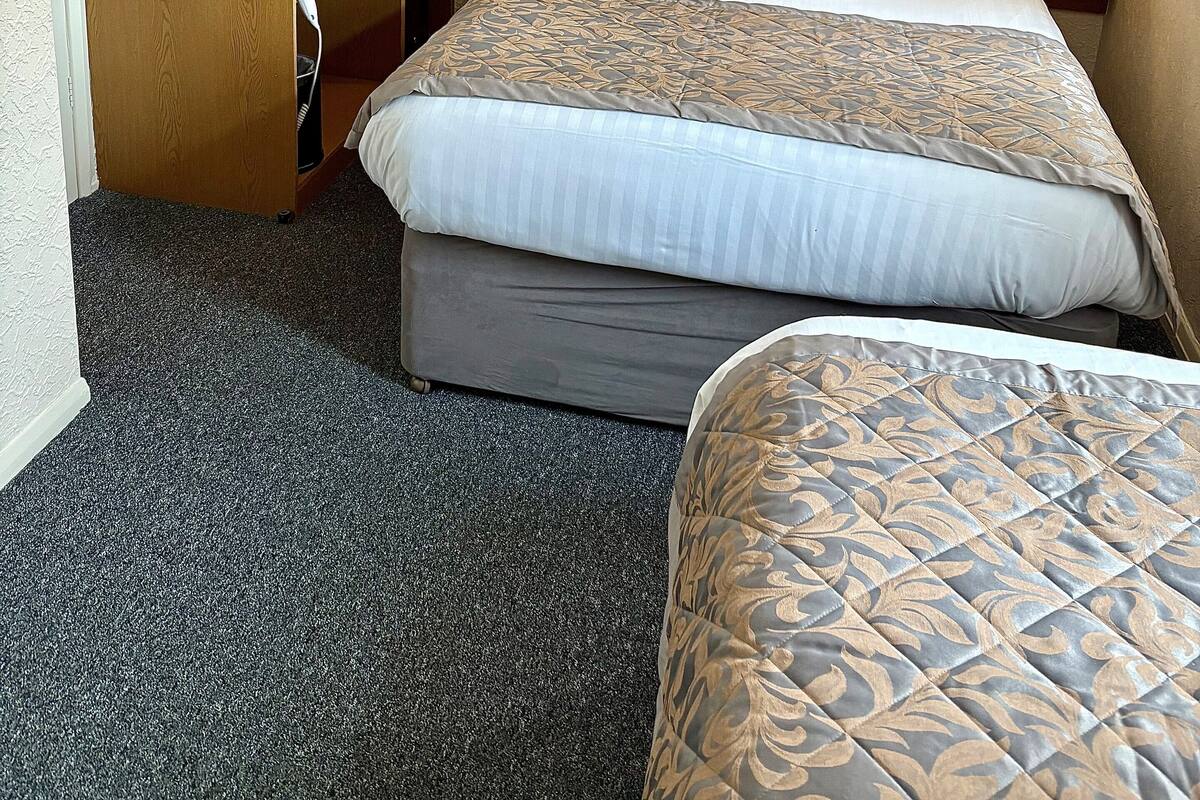 A hotel room with a bed, a desk with a chair, a small table, a microwave, a coffee maker, and a painting of beach huts.