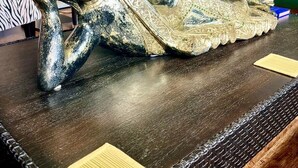Una estatua dorada decorativa sobre una mesa de madera en una habitación con una silla verde y una planta al fondo.