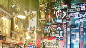Un bar de temática retro con cabinas verdes, una mesa redonda de madera y paredes decoradas con diversos carteles y recuerdos antiguos.