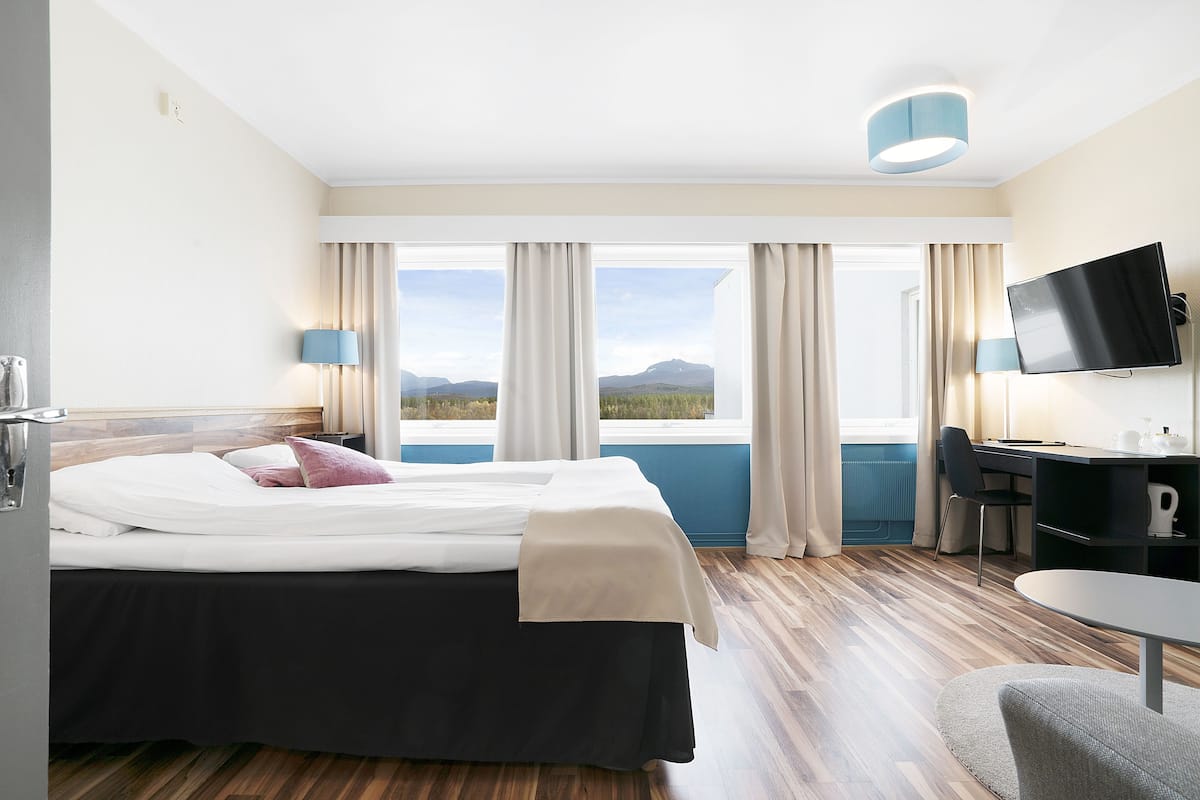 Habitación de hotel con cama, escritorio, silla, televisor y vista a las montañas.
