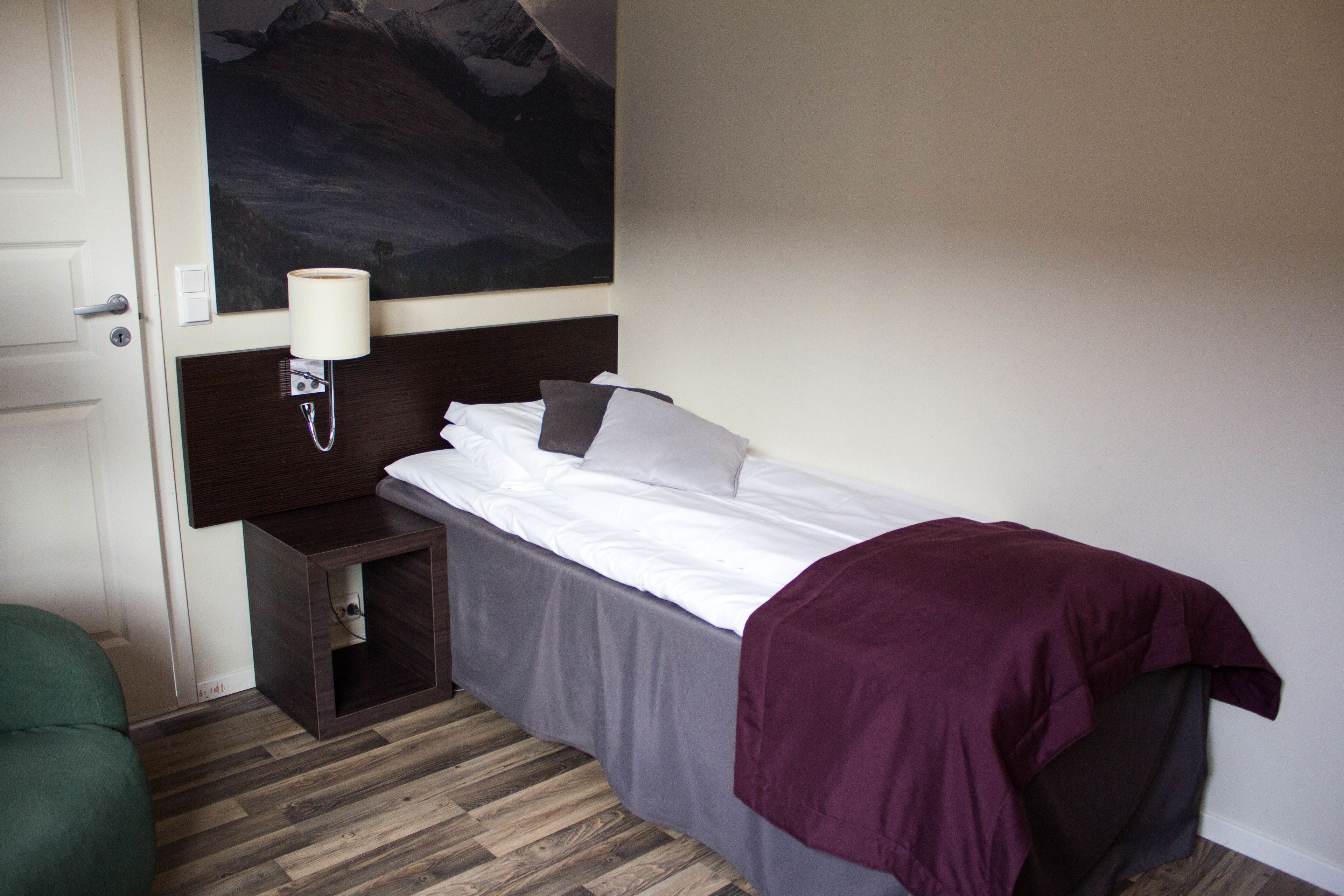 A hotel room with a bed, a nightstand, a lamp, and a painting on the wall.