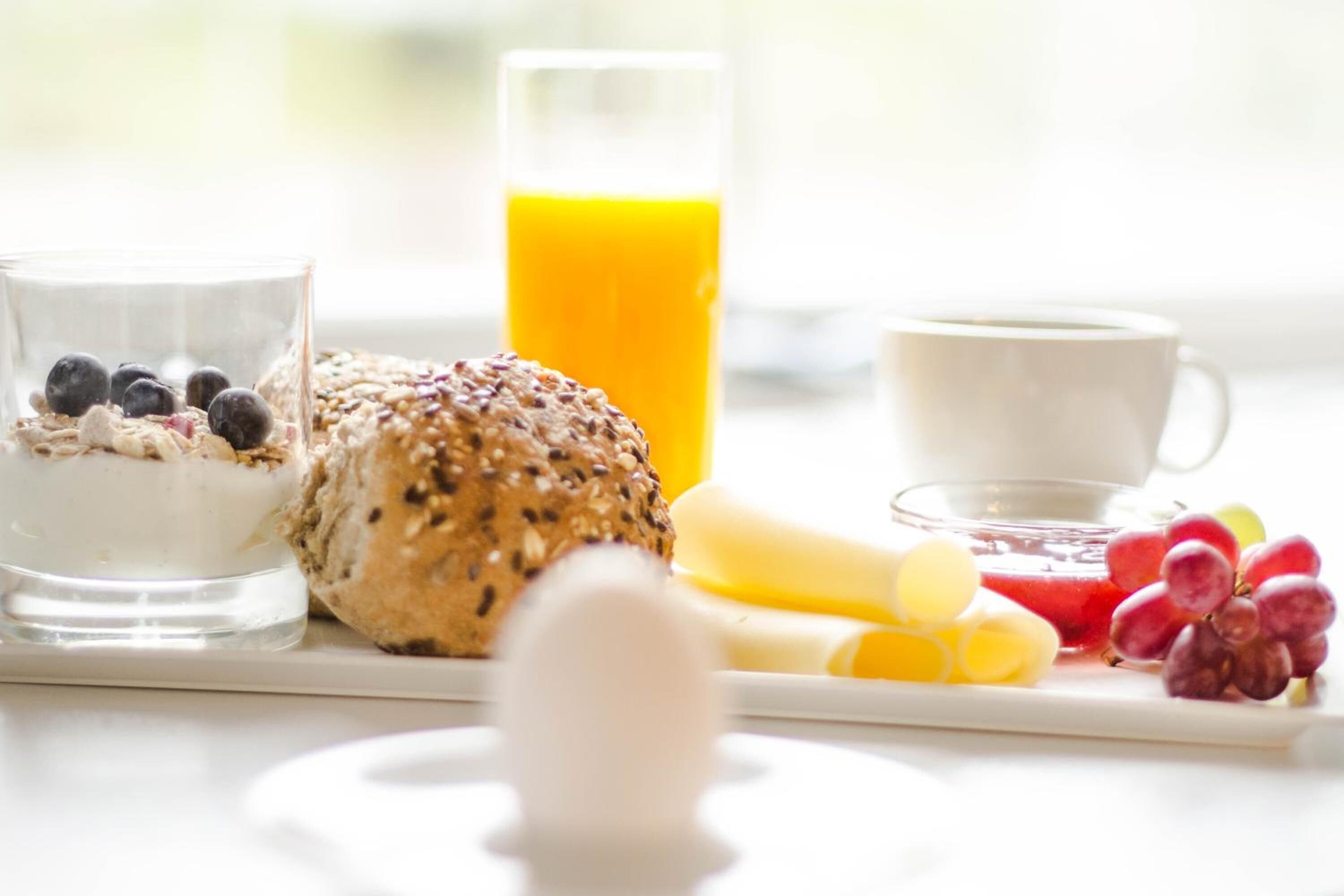 A breakfast setting with a glass of milk, a bowl of cereal with blueberries, a slice of bread, a glass of orange juice, a cup of coffee, and various fruits.