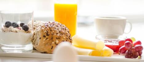 A breakfast setting with a glass of milk, a bowl of cereal with blueberries, a slice of bread, a glass of orange juice, a cup of coffee, and various fruits.