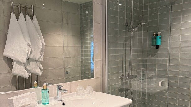 A modern bathroom with a large mirror, a white sink, and a glass-enclosed shower. - Bardufoss Hotell (Målselv)