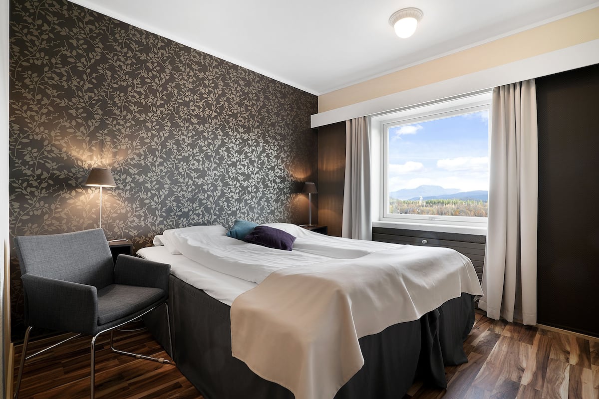 Una habitación de hotel con cama, una silla, una lámpara y un ventanal con cortinas.