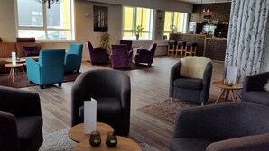 A spacious lounge area with multiple seating options including armchairs and sofas, a bar area with a counter and bar stools, and large windows providing natural light. - Bardufoss Hotell (Målselv)