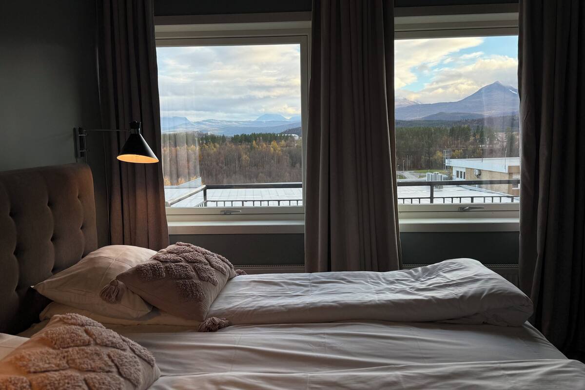Habitación de hotel con cama, lámpara y ventana que ofrece vistas a montañas y árboles.