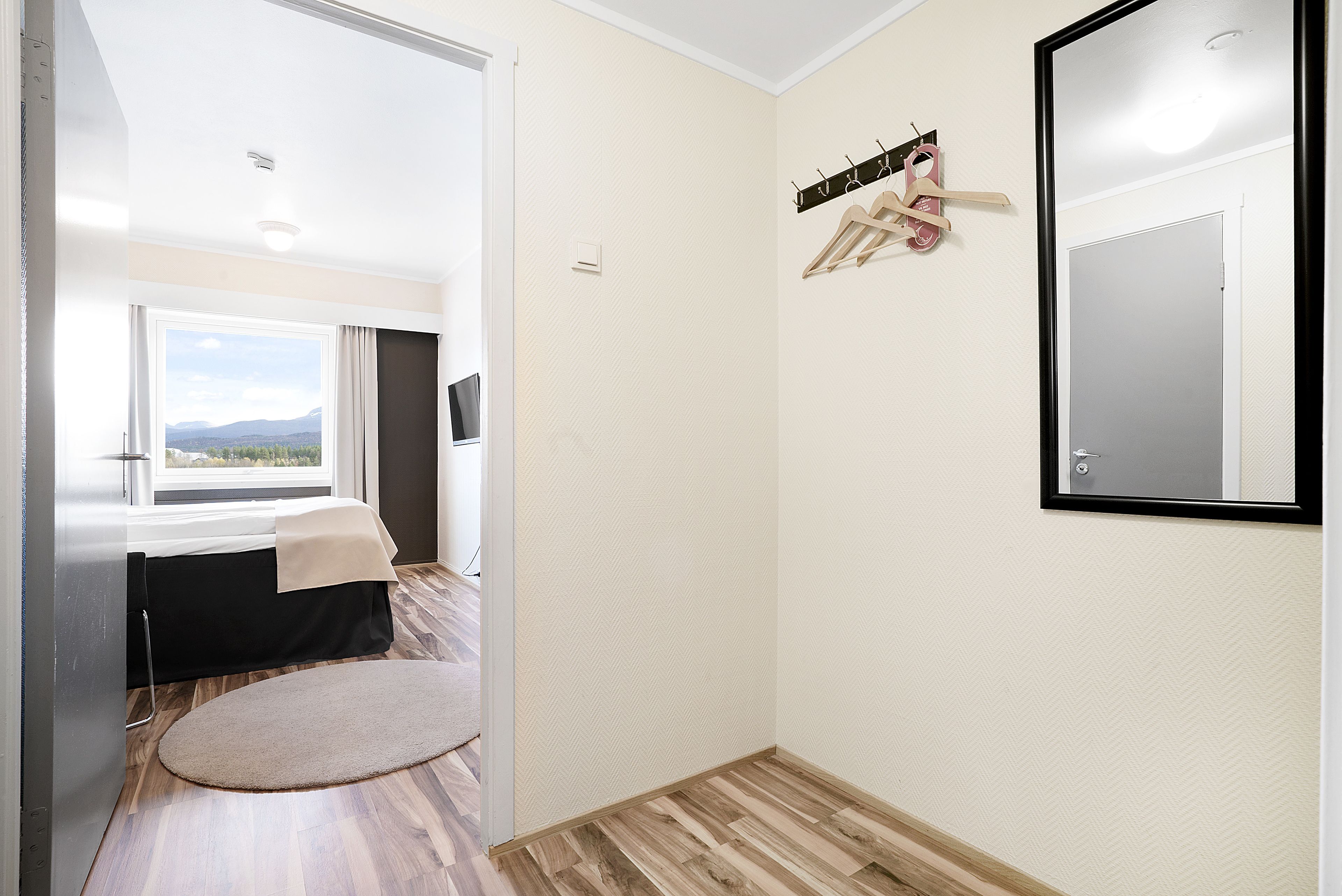 Une chambre d’hôtel avec un lit, une fenêtre donnant sur un beau paysage, un porte-manteau et un miroir.