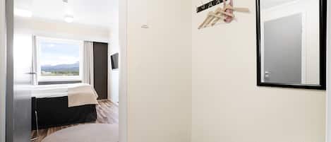 Una habitación de hotel con cama, ventana con vistas, perchero y espejo.