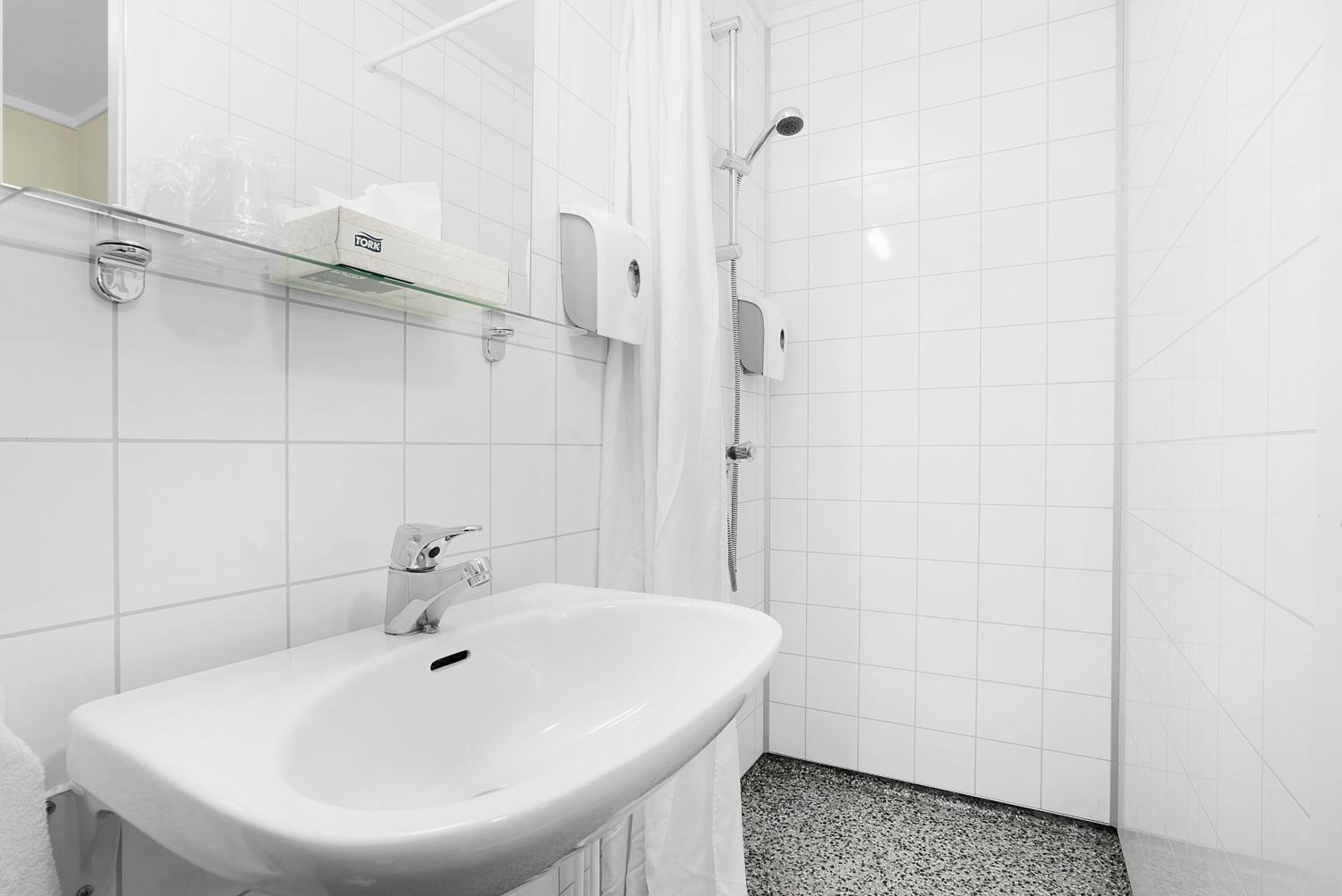 A modern bathroom with a white sink, a glass shelf with toiletries, and a shower area.