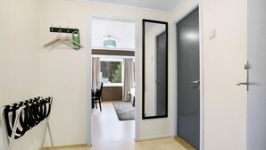 A hallway with a coat rack, a door, and a view into a room with a table and chairs. - Bardufoss Hotell (Målselv)