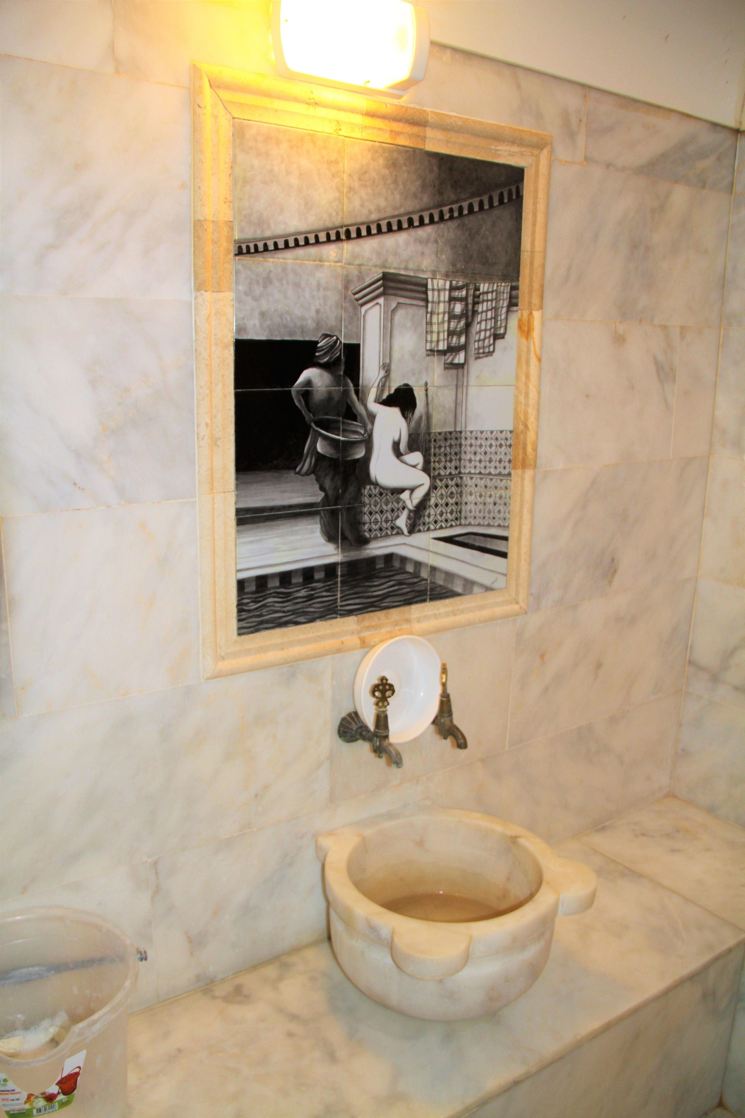 A bathroom with a marble sink, a framed black and white photograph on the wall, and a light fixture above the mirror.