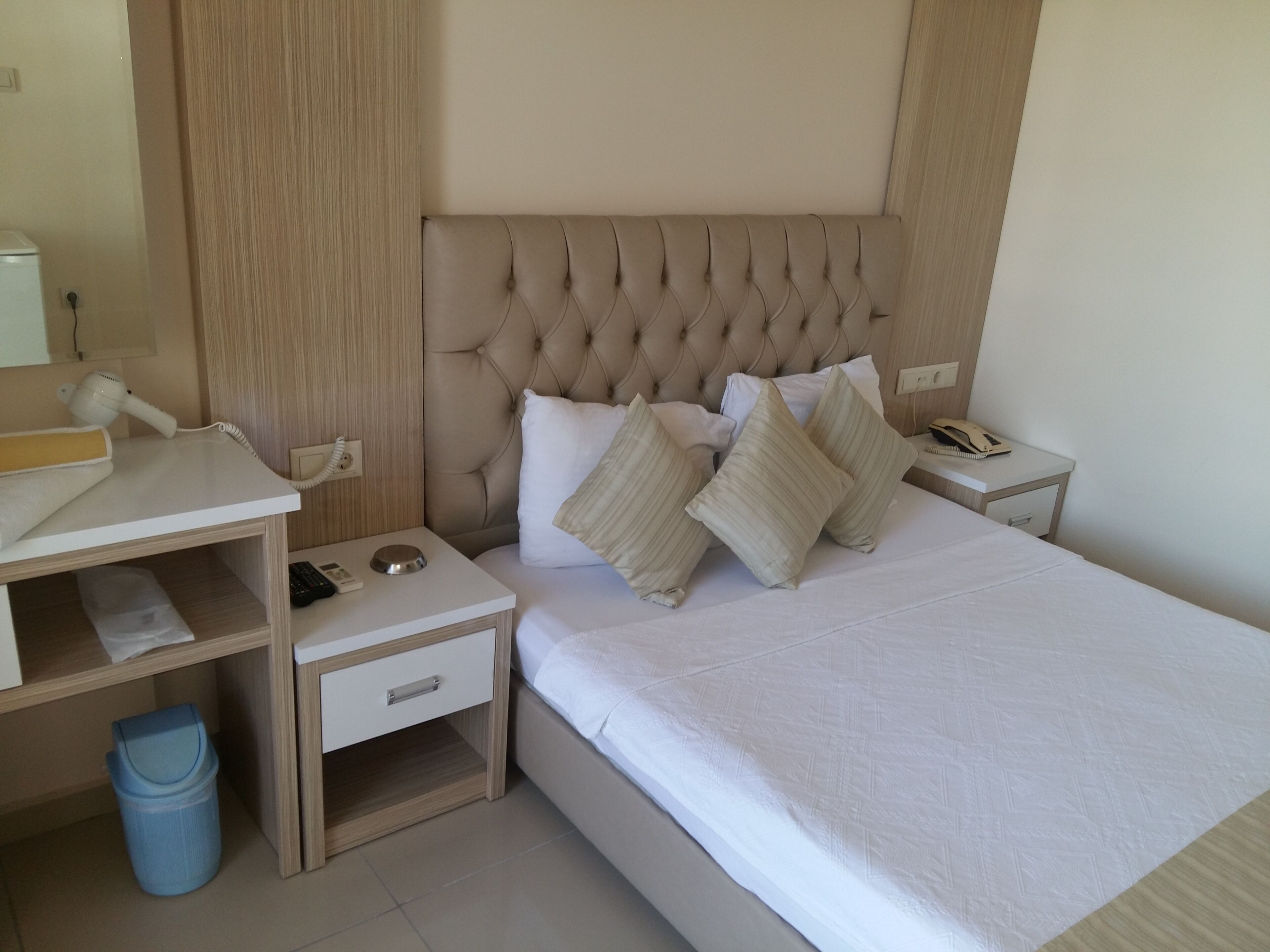 A bedroom with a tufted headboard, a bedside table with a lamp, a phone, and a trash bin.
