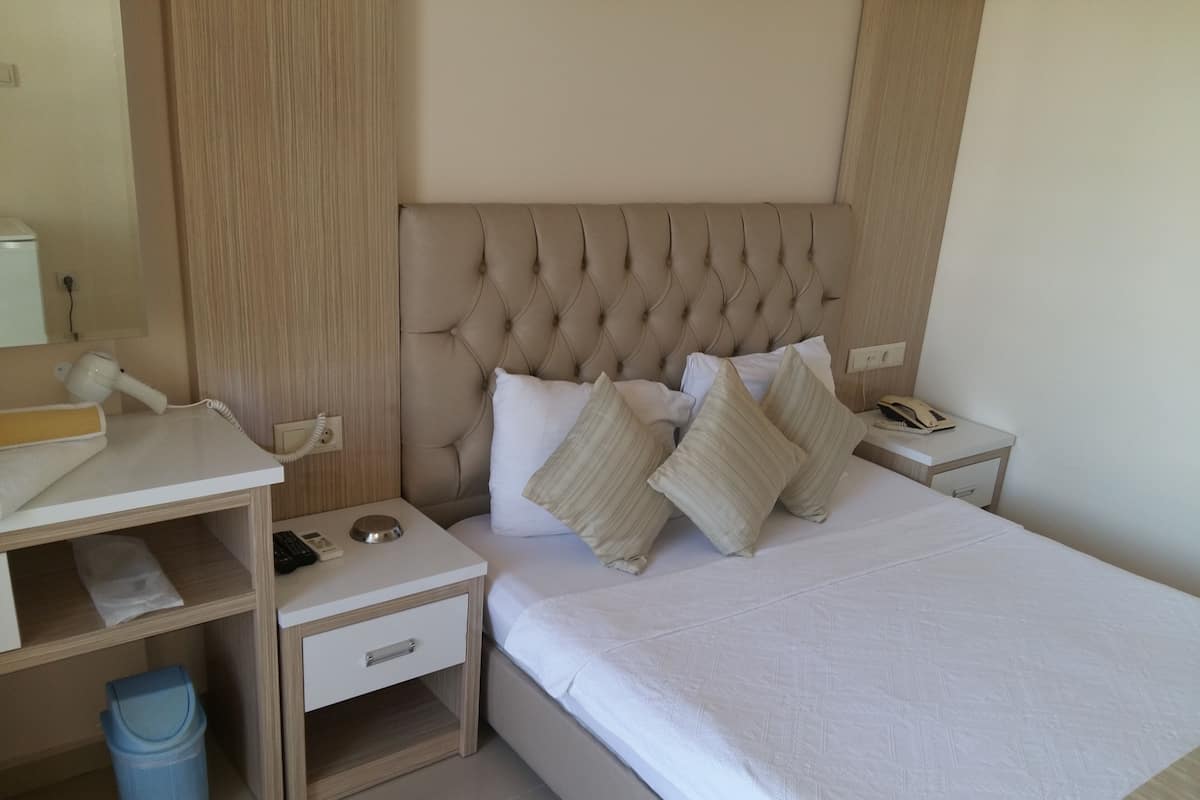 A neatly arranged hotel room with a tufted headboard, a bedside table with a lamp, a phone, and a trash bin.