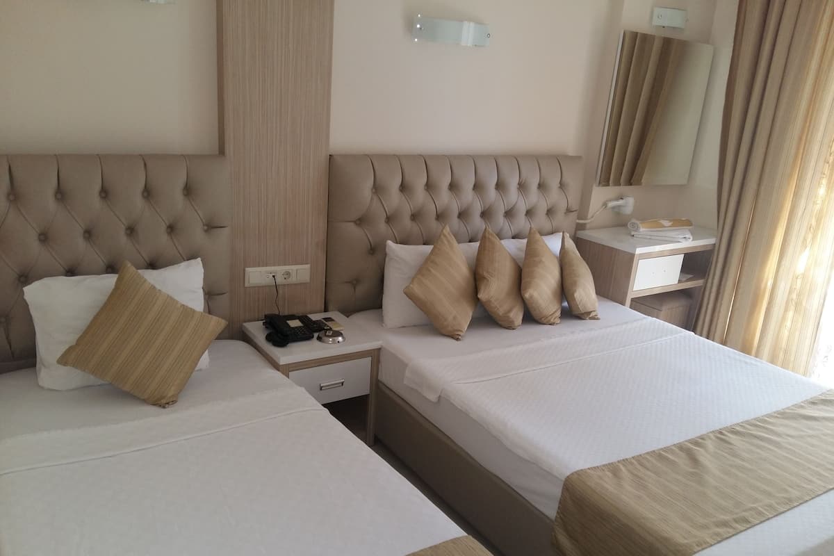 A hotel room with two beds, a bedside table with a phone and remote, a nightstand, a mirror, and a window with curtains.