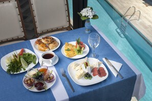 A dining table with various dishes, a glass of water, and a vase with flowers by a poolside. - Temple Hotel (Didim)