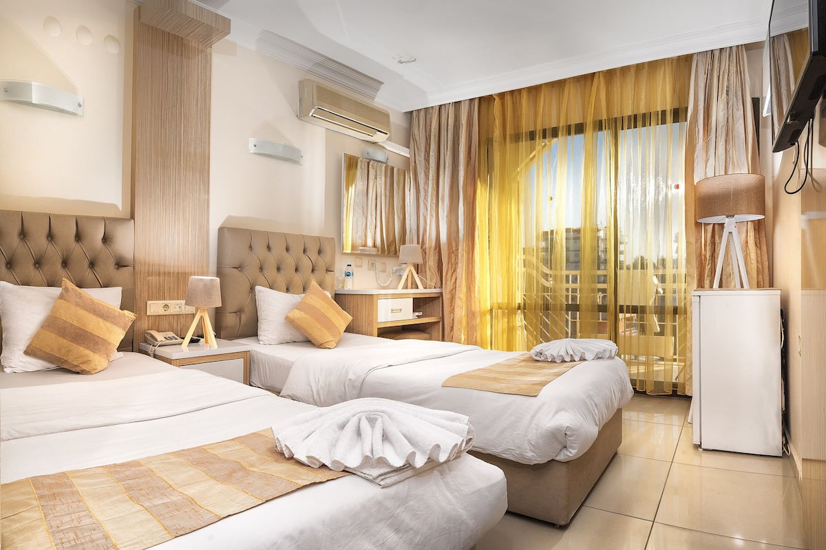 A hotel room with two beds, a minibar, a TV, and a large window with curtains.