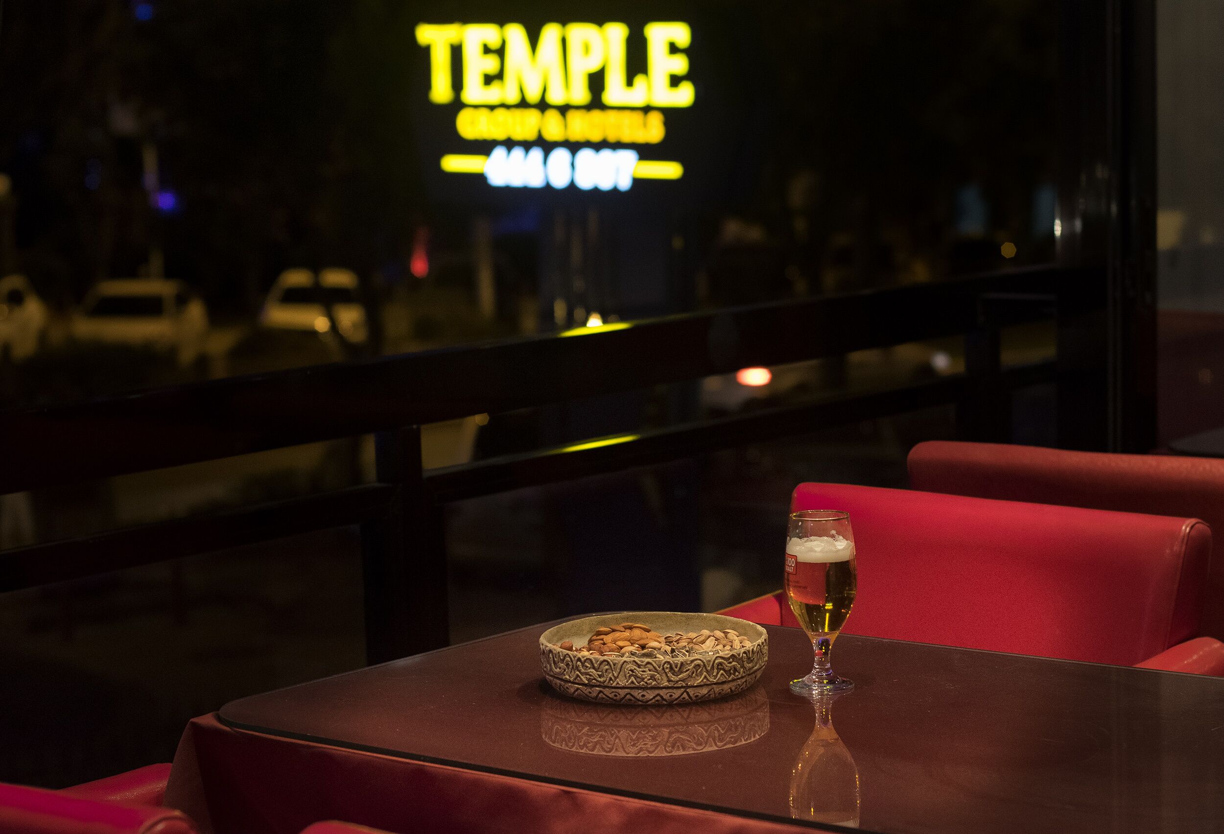 Een restaurant met een neonreclame, een tafel met een schaal noten en een glas bier.