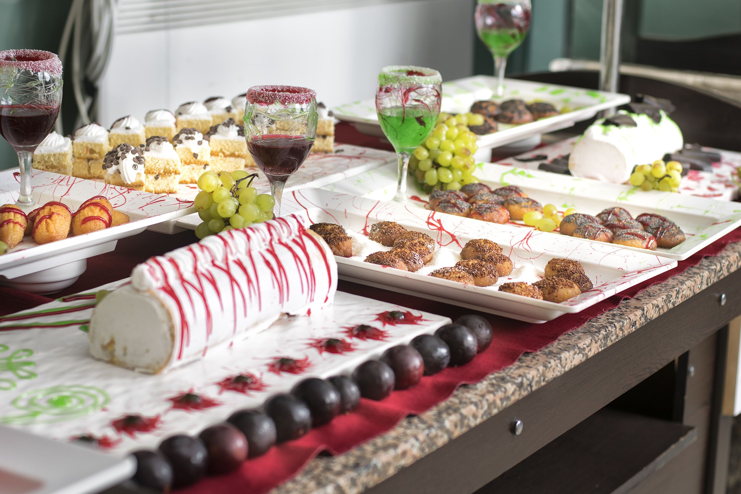 Uma mesa de buffet com diversos doces, incluindo bolos, pâtisseries e um bolo branco grande com cobertura vermelha.
