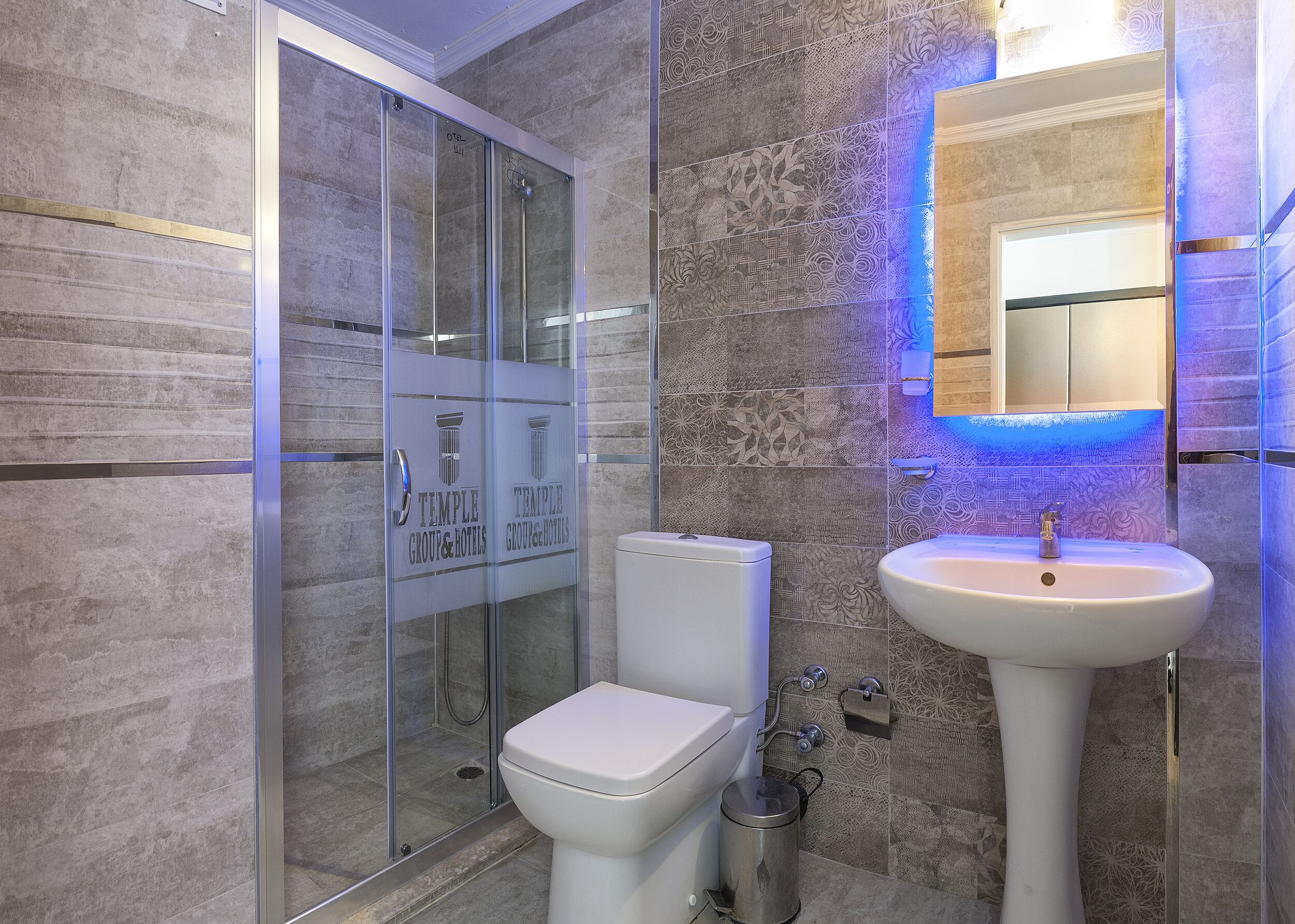 A modern bathroom with a glass shower enclosure, a white toilet, and a pedestal sink with a mirror.