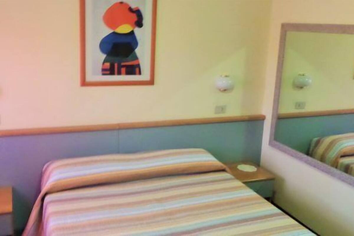 A hotel room with a single bed, a bedside table, a mirror, and a wall-mounted light fixture.