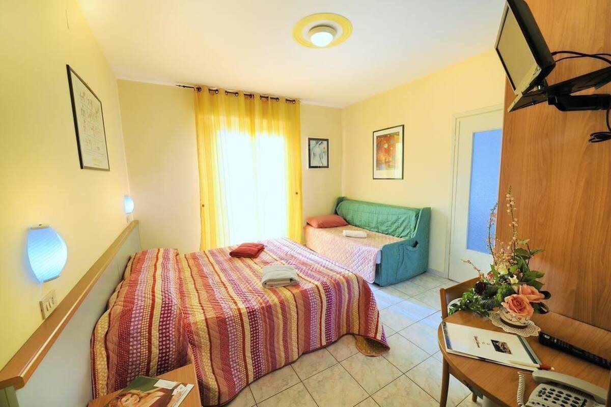 A hotel room with a bed, a desk with a telephone, and a window with curtains.