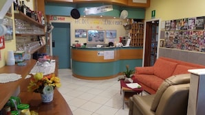A hotel reception area with a curved counter, a sofa, and a wall decorated with photographs. - Hotel Lucerna (Taggia)
