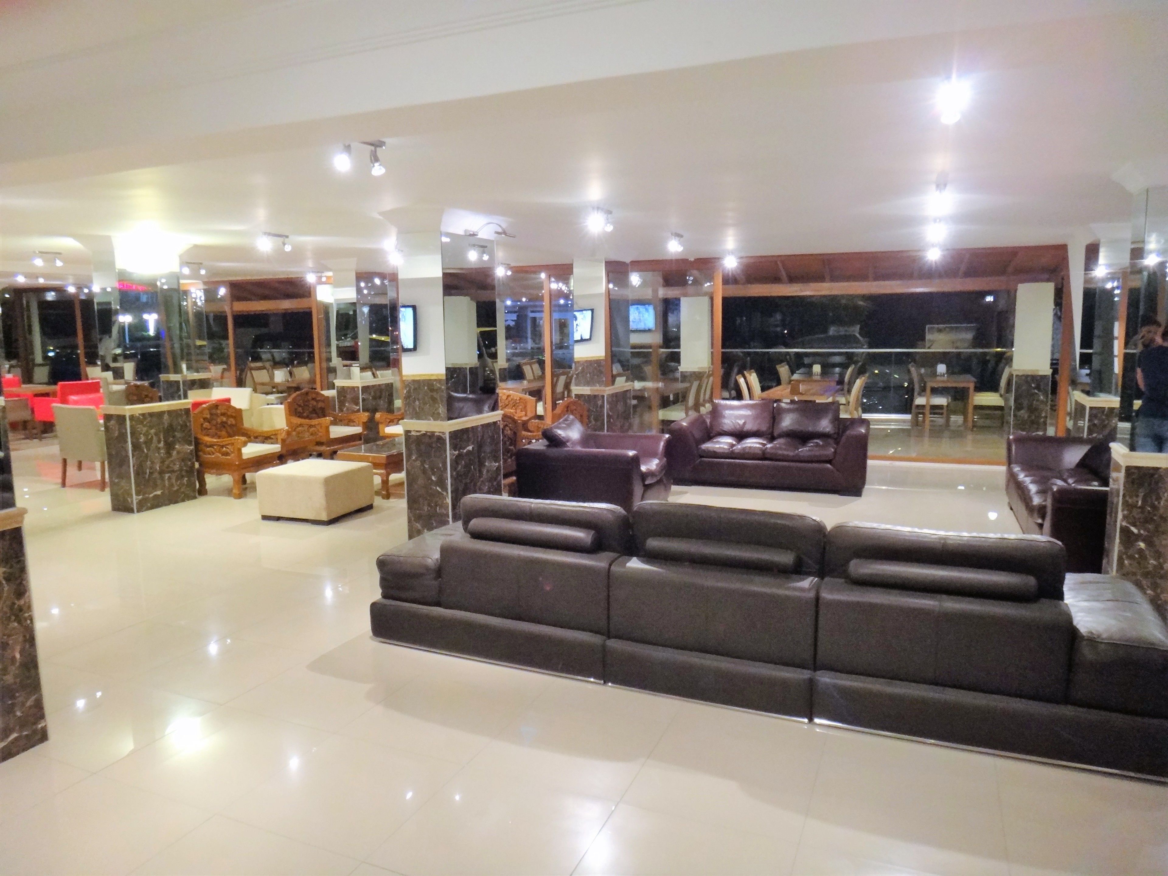 A spacious lobby with a large dark sofa, wooden chairs, and a marble reception desk.