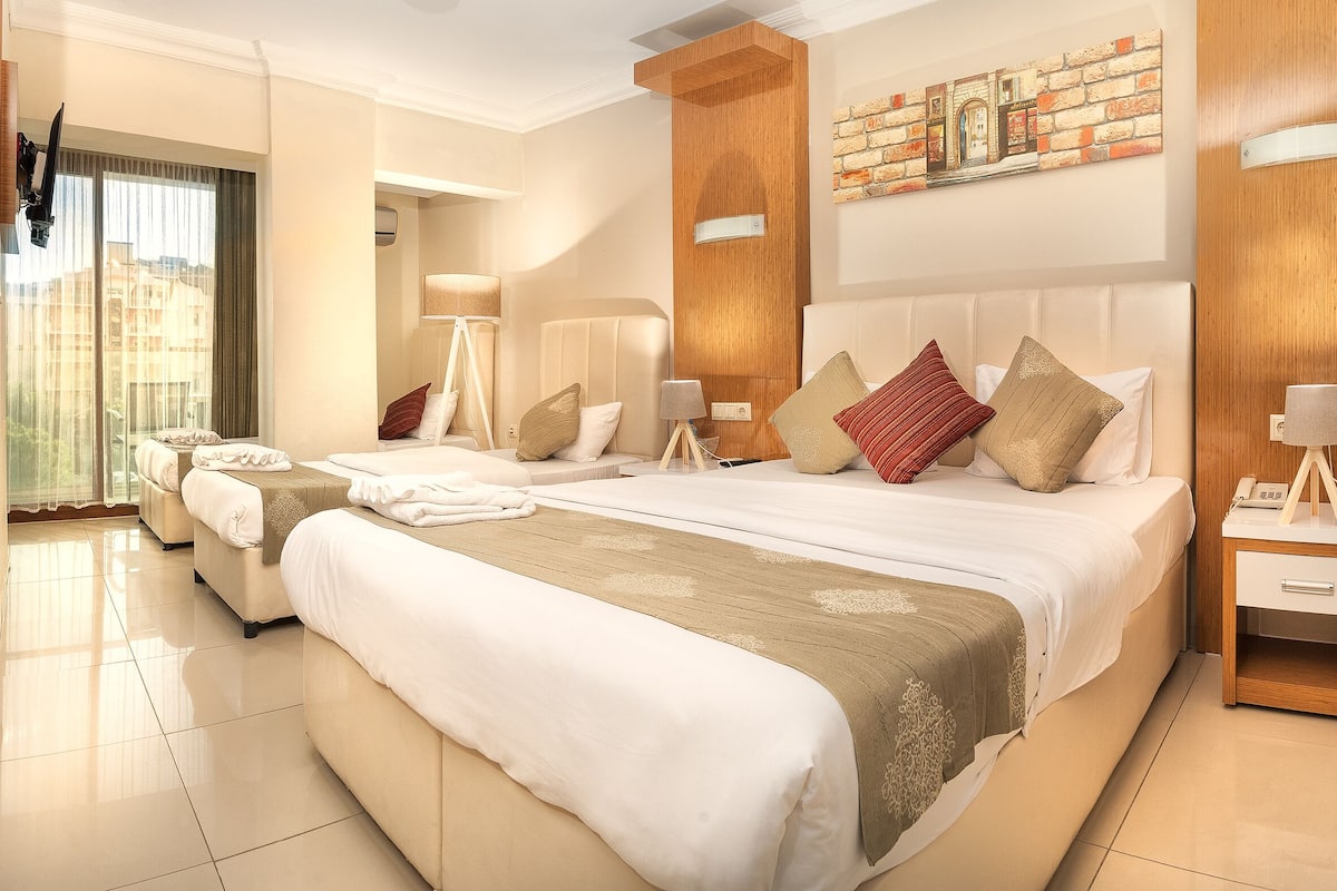 Habitación de hotel con una cama grande, mesitas de noche, una lámpara y vistas al exterior.