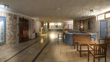 A spacious indoor area with a pool, wooden furniture, and tiled walls.