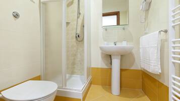 A bathroom with a toilet, shower, sink, and a hairdryer mounted on the wall.